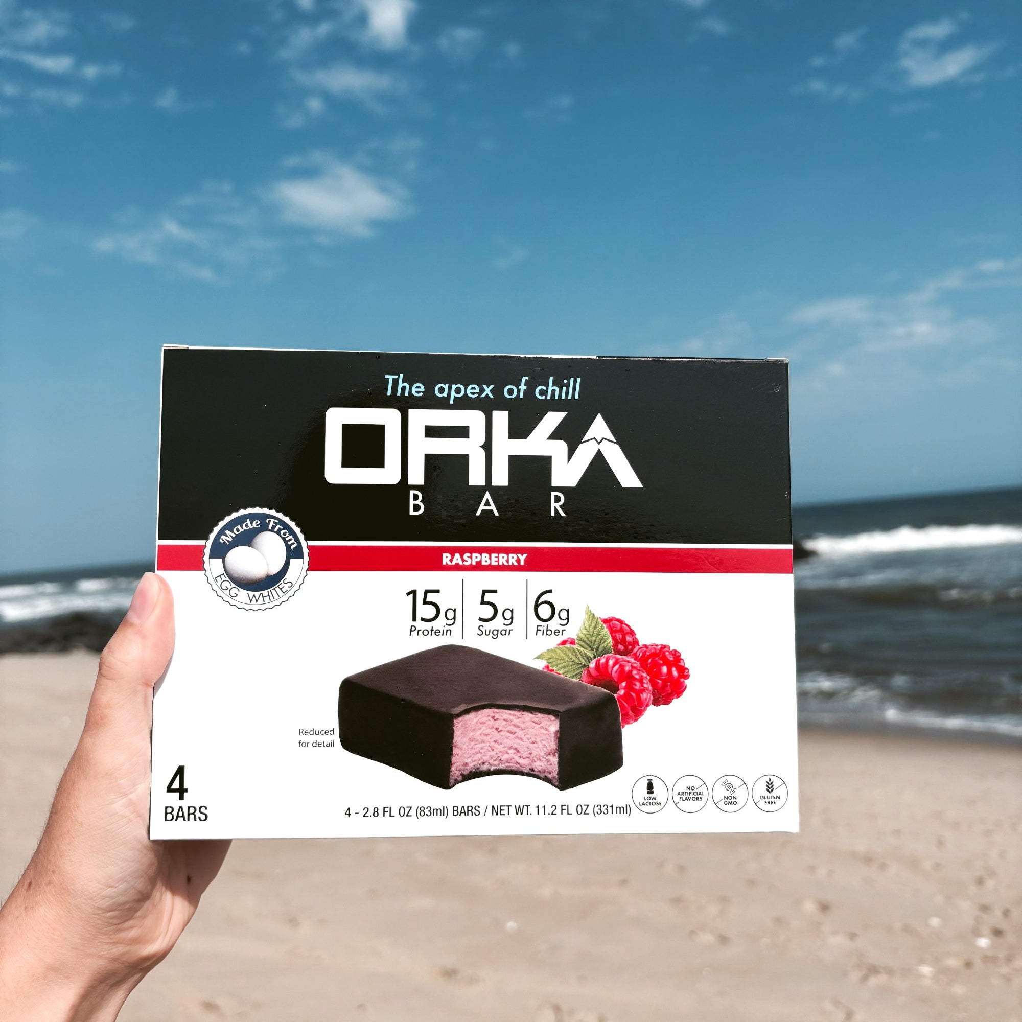 Orka Bar Raspberry Packaging holding in front of ocean on beach