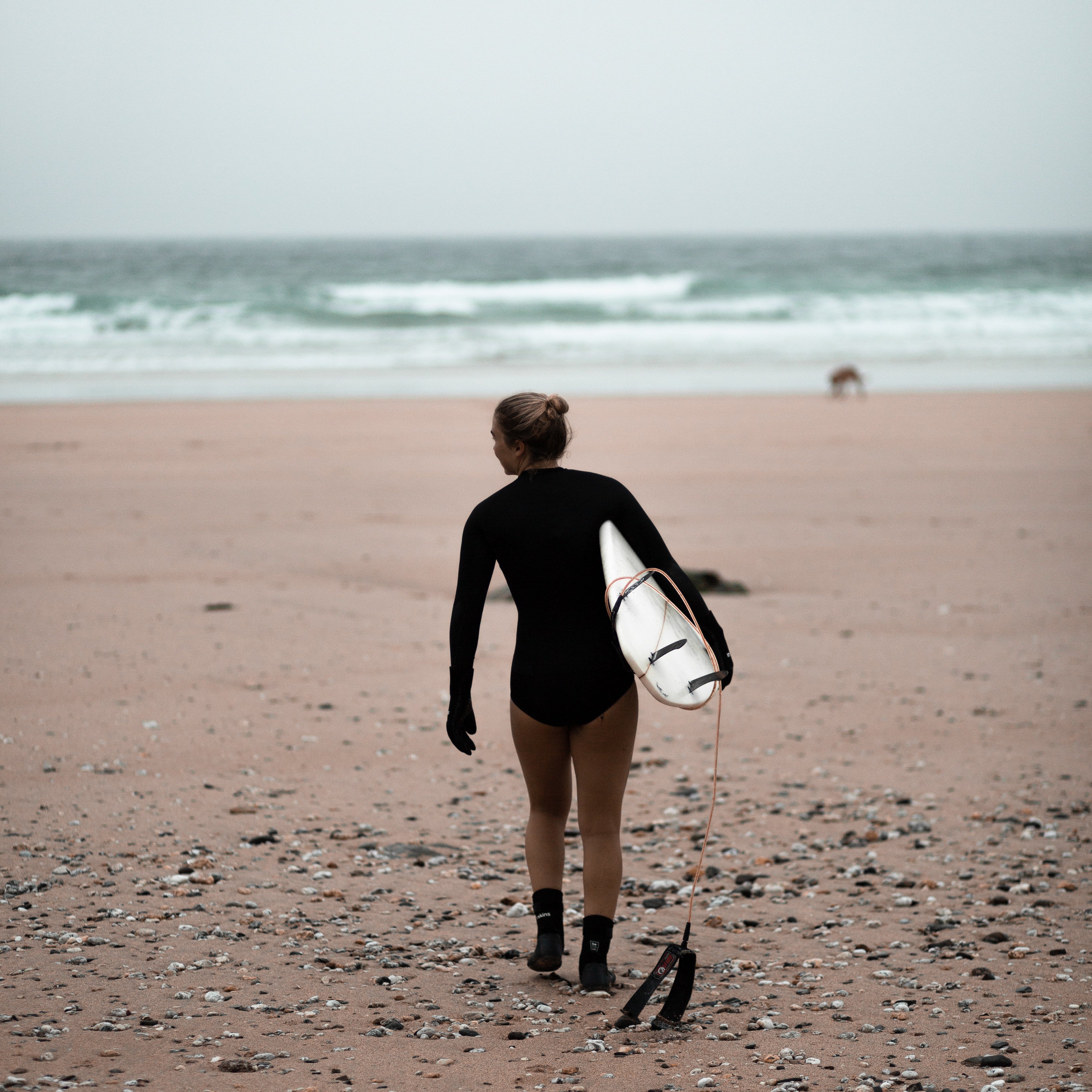 Person carrying surfboard on beach towards ocean